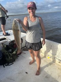 An excited angler proudly displaying a large Redfish while fishing on a boat in a scenic waterway.