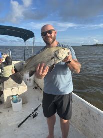 An angler proudly displaying a large Black Drum while fishing on a boat in a scenic waterway.