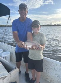 A proud grandfather and grandson duo displaying a Redfish on a fishing trip, with a scenic water backdrop.