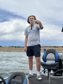 A young angler proudly displaying a caught fish while standing on a boat, enjoying a day of fishing on a lake.