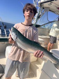 A young angler proudly displaying a large Silver Salmon aboard a fishing boat, enjoying a sunny day on the water.