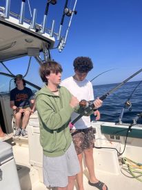 Two young anglers engaged in fishing on a boat, with rods in hand and the ocean in the background.