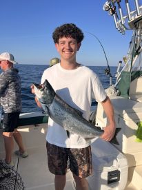 A young angler proudly displaying a large Salmon while fishing on a boat in open waters.