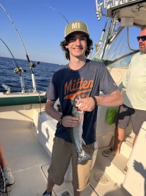 A young angler proudly displaying a freshly caught fish aboard a fishing boat, enjoying a sunny day on the water.