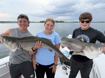 Three young anglers proudly displaying their catch of striped bass while on a fishing trip.