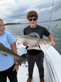 Two young anglers proudly displaying their catch of striped bass while fishing on a boat, showcasing a fun day on the water.