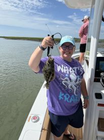A young angler proudly displaying a Flounder while fishing on a boat in a coastal waterway.