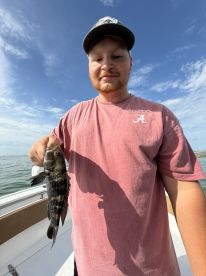 Angler holding a Black Drum while fishing on a boat, enjoying a sunny day on the water.