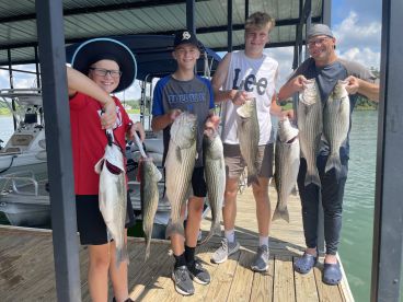 A group of young anglers proudly displaying their catch of striped bass at a dock after a successful fishing trip.