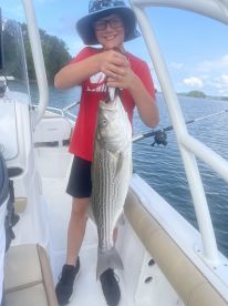 A young angler proudly displaying a striped bass while fishing on a boat, showcasing a successful day on the water.
