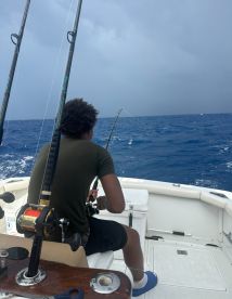 A young angler focused on reeling in a catch while fishing offshore, surrounded by open water and a cloudy sky.