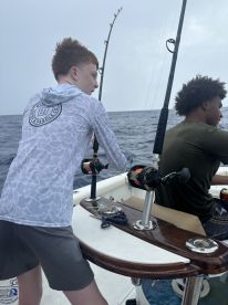 Two young anglers engaged in fishing on a boat, with rods in hand, showcasing the excitement of deep-sea fishing.