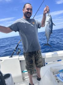 An angler proudly displaying a large Bonito while fishing offshore, showcasing a sunny day on the water.