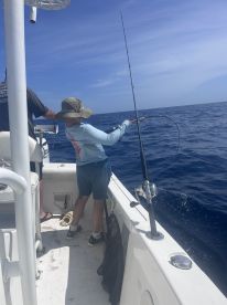 A young angler actively reeling in a fish while fishing on a boat in open water, showcasing the excitement of deep-sea fishing.
