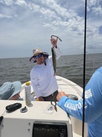 An angler proudly displaying a Speckled Trout while fishing on a boat in coastal waters, showcasing a sunny day and a relaxed atmosphere.