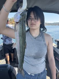 A young angler proudly displaying a Rainbow Trout while fishing on a boat, showcasing a beautiful day on the water.