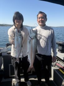 Two anglers proudly displaying their catch of large trout while fishing on a scenic lake.