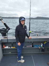 A woman stands inside a fishing boat, dressed for the weather, with fishing gear visible in the background, showcasing a typical fishing environment.