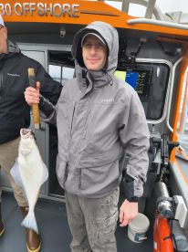 An angler proudly displaying a freshly caught Halibut aboard an offshore fishing boat, showcasing the excitement of a successful fishing trip.