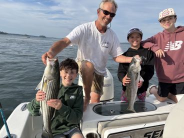 A group of young anglers proudly displaying their striped bass catch on a fishing charter, enjoying a day on the water.