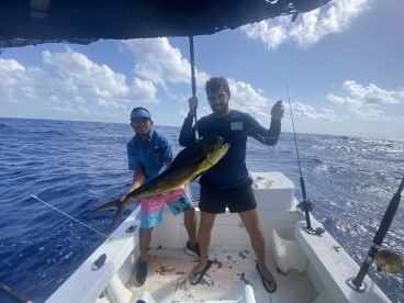 Two anglers on a boat proudly displaying a large Mahi Mahi while fishing in open waters.