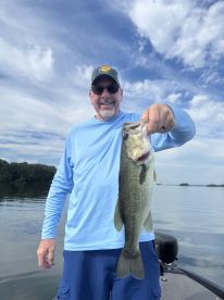 An angler proudly displaying a large Largemouth Bass while fishing on a calm lake, showcasing a beautiful day on the water.