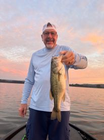 An angler proudly displaying a large Largemouth Bass during a serene sunset fishing trip on a lake.