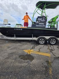 A man stands on the side of a sleek fishing boat named 'Kat D' at the dock, showcasing its vibrant green accents and spacious seating, ideal for a day out on the water.