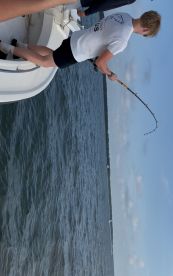 A young angler is actively reeling in a fish while fishing from a boat in a scenic waterway.