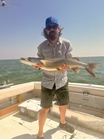 Angler proudly displaying a large Northern Pike while fishing on a sunny day in open waters.