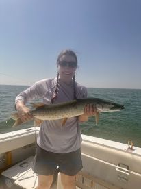 Angler proudly displaying a large Muskellunge while fishing on a boat, showcasing a sunny day on the water.