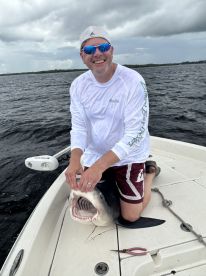 An angler kneeling on a boat, proudly displaying a large shark while enjoying a fishing trip.