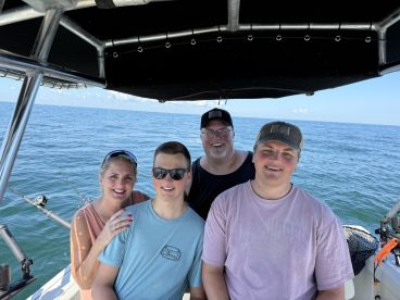A family enjoying a day on the water, posing inside the boat with a scenic ocean backdrop.