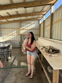 A young woman joyfully poses with a large fish in a cleaning station, showcasing her catch after a successful fishing trip.