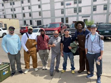 A group of anglers posing together in a parking area, likely after a fishing trip, showcasing camaraderie and excitement.