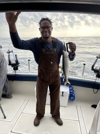 Angler proudly displaying a freshly caught fish aboard a fishing boat, with a serene ocean backdrop.