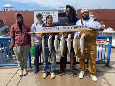 Group of anglers proudly displaying their catch of Lake Trout on a catch board at the dock, showcasing a successful fishing trip with Chasin' Tail Charters in Minnesota.