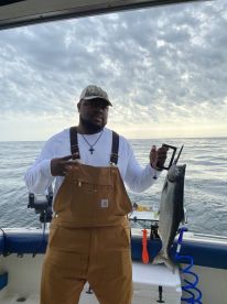 Angler proudly displaying a freshly caught Salmon while aboard a fishing boat, with a scenic ocean backdrop.