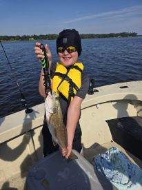 A young angler proudly displaying a freshly caught striped bass while fishing on a sunny day.