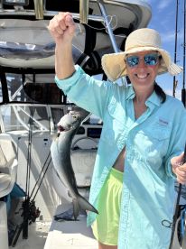 A smiling angler proudly displaying a freshly caught fish aboard a boat, showcasing a sunny day on the water.