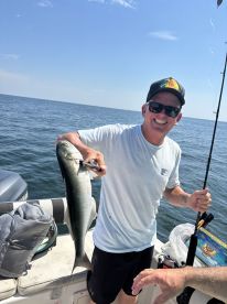 Angler smiling while holding a large fish on a boat in open water, showcasing a successful fishing trip.