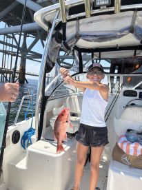 A young angler proudly displaying a Red Snapper while fishing from a boat, showcasing a fun day on the water.