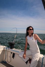 A woman is actively fishing on a boat, showcasing the excitement of reeling in a catch on a sunny day at sea.