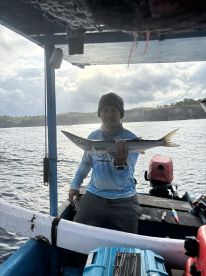 Angler proudly displaying a large fish while aboard a small fishing boat, with a scenic coastal backdrop.