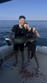 Two young anglers proudly displaying a large fish on the deck of a boat during a successful fishing trip.