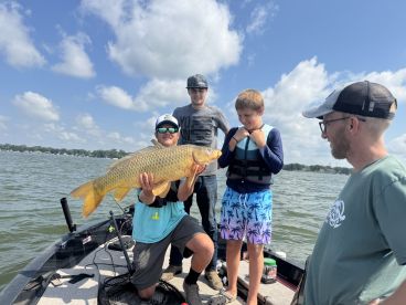 A group of anglers celebrating a successful catch of a large carp while out on a boat, showcasing a fun family fishing experience.