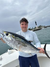 An angler proudly displaying a large Yellowfin Tuna while fishing near a lighthouse, showcasing a successful offshore trip.