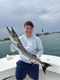 A proud angler displaying a large Barracuda while fishing off the coast, with a lighthouse visible in the background.