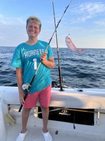 Young angler proudly displaying a freshly caught fish while fishing on a boat in open waters.