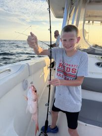 A young angler proudly displaying a Red Snapper while fishing on a boat, showcasing a successful catch during a family outing.